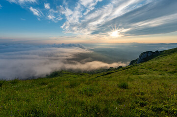Fototapeta na wymiar Green meadows with rocks and rocky mountains with fog in the valley and clouds in the sky in romanian mountains in muntii ciucas