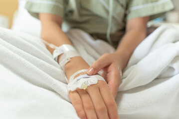 Young patient asian woman lying on bed in hospital with IV saline drip to back of the hand, teenager sick in hospital, Selective focus, healthcare and health insurance concept.
