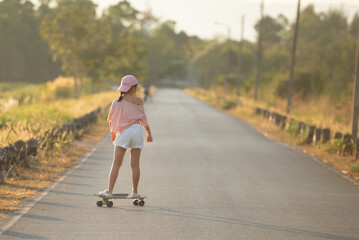 Teenager Beautiful happy Asian healthy woman smiling,riding and playing extreme sports skateboard as outdoor activity with happiness, relaxation during holidays in summer vacation at park morning time