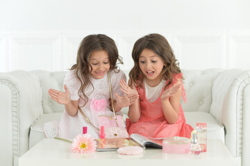 Obraz na płótnie Canvas Cute sisters sitting on sofa with magazine and cosmetics