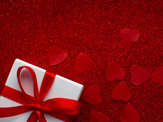 White gift box is on red heart paper background, top view. Greeting card, present. Valentines day holiday concept. Flat lay with a lot of tiny heart-shaped papers with space for text. February 14th.