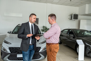 Young male client choosing new car with salesman at modern salon