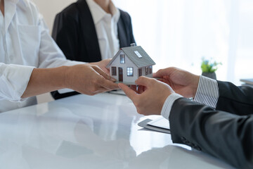 Young Asian real estate agent, and insurance salesman handing over a sample house to a client after...