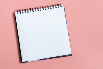 Mock up of empty spiral sketchbook with white paper on pastel pink background. Top view of open notebook with clean sheet. Template for message. Copy space.