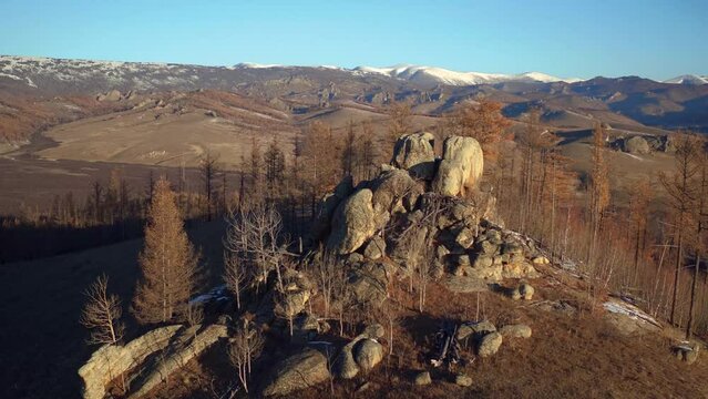 Panoramic shot of a tree-covered rock formation on top of a hill in a dry and mountainous landscape. Ulaanbaatar, Tov Province in Mongolia