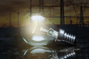 close up of tungsten light bulb with glow on dark polished marble surface and background of high voltage electricity power lines
