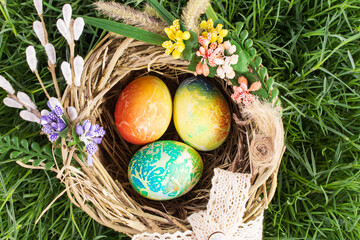Colored eggs in nest with flowers on grass. View from above. Easter, Egg Hunt
