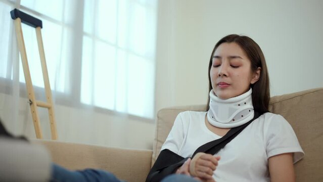 Happy woman recovery from accident fracture broken bone injury with leg splints in cast, neck splints collar, arm splints, sling support arm in living room. Social security and health insurance.