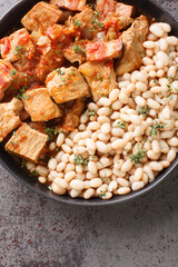 Spicy pork stew with bacon, tomato and onion with a side dish of white beans close-up in a plate on the table. Vertical top view from above