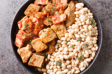 Roast pork with bacon, tomato and onion with white bean garnish close-up in a plate on the table. Horizontal top view from above
