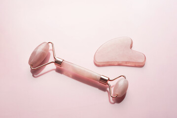 Close-up quartz roller and gua sha massage scraper on pink background. Facial massage tools. Skin care, beauty and health concept.