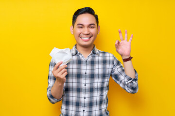 Happy young handsome Asian man in casual clothes holding tissue paper and showing okay gesture...