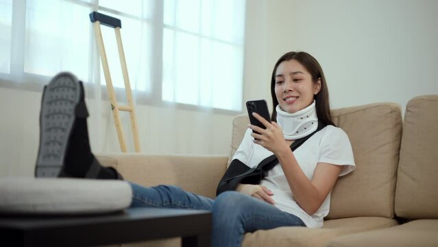 Woman recovery from accident fracture broken bone injury with leg splints in cast, neck splints collar, arm splints, sling support arm using smartphone. Social security and health insurance concept.