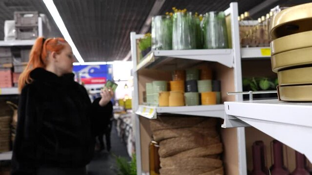Shelves in a store with interior and home decor items. In the background, out of focus, a girl chooses a glass flowerpot.
