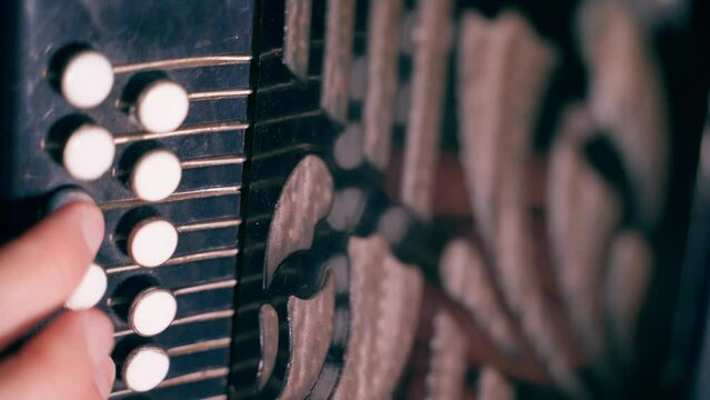 Fingers press the accordion buttons close-up. Playing an old musical instrument with white keys