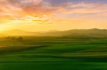 beautiful sunset or sunrise in rural countryside green hills with farm and mountains on background