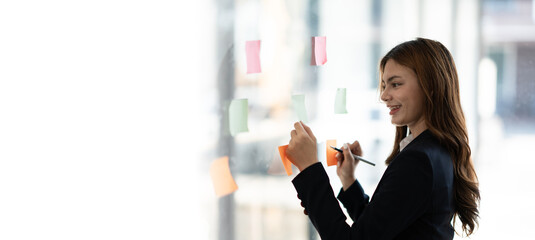 Young charming businesswoman writing new ideas on sticky note in the meeting room.