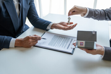 Asian young businessman, insurance sales agent handing keys to the client after signing a contract for the purchase or renting the house on the desk in new location, moving concept new beginning.