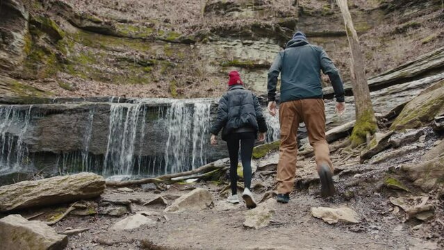 Man and woman discover waterfall and walk on rocks taking it in