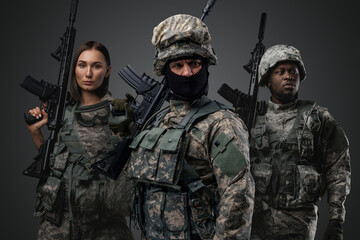 Shot of brave military people dressed in uniform holding rifles against gray background.