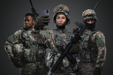 Shot of soldier woman talking on smartphone near comrades against gray background.