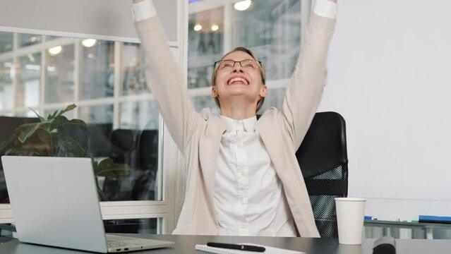 Good news on smartphone, moment of victory great sms receive. Office worker in glasses sits at desk holds phone read e-mail celebrates success career advance, hiring of job of dream, raise hands up.