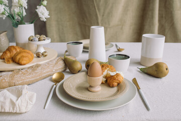 Egg on a stand, classic croissant with cream cheese. Delicious breakfast at home. Table setting for family Easter meal.