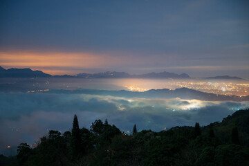 Night view of city lights in the valley. Spectacular cloud waterfall in the sky. The sea of clouds landscape. Dahu Township, Miaoli County, Taiwan