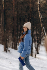 A pretty young woman in a stylish blue jacket holds a cup in her hands. A warm, soft, cozy image.