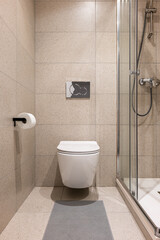 Toilet with walls and floor in soft beige square tiles. The white toilet creates the effect of...