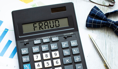 A calculator labeled FRAUD lies on financial documents in the office.