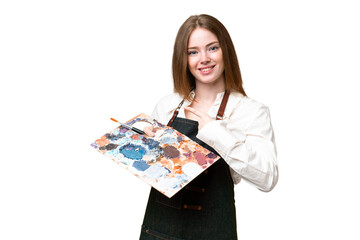 Young artist woman holding a palette over isolated chroma key background pointing to the side to...