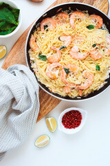 top view of pan with cooked creamy basil shrimp pasta with pink pepper and lime, white background