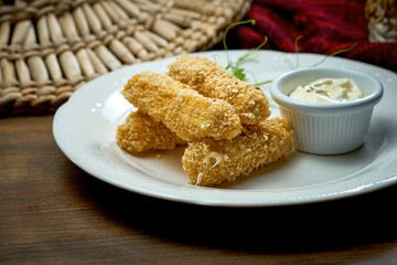 Fried mozzarella sticks in breading with sauce in a white plate. Wooden background