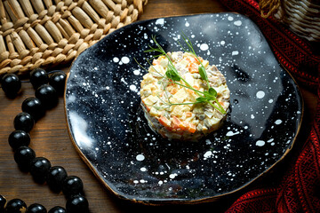 Olivier salad with chicken, pickles and mayonnaise in a plate on a wooden background