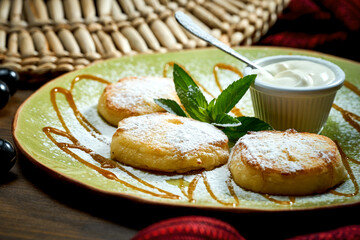 Ukrainian syrnyky with sour cream and powdered sugar in a plate. tasty cottage cheese pancakes