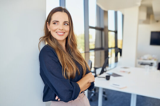 Contemplative businesswoman with arms crossed leaning on wall at office