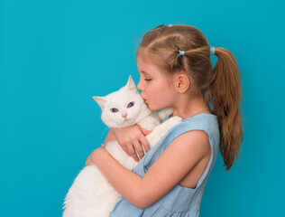 Little girl kissing her white cat over blue background.