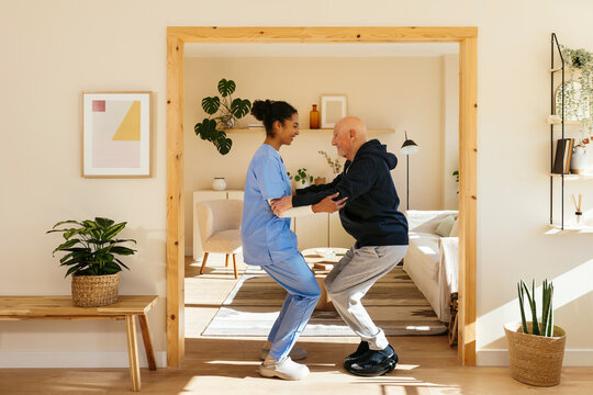 Home caregiver assisting senior man in exercising at home