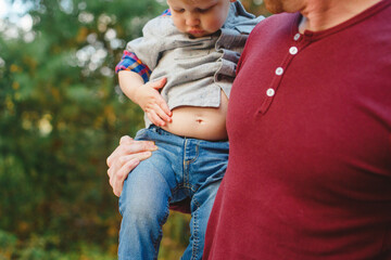 Close-up of a toddler in father's arms investigating his exposed belly