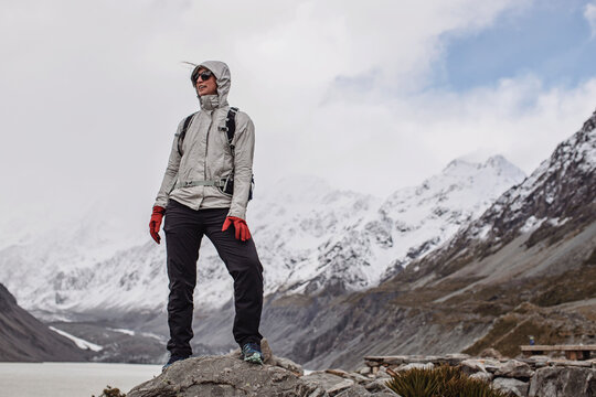 cold woman stands on rock while hiking to Hooker Valley New Zealand