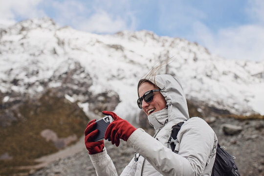 Woman hiker with uses cell phone camera on windy day in mountains.