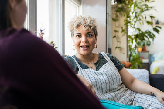 Mid adult woman talking to friend while sitting on sofa at home