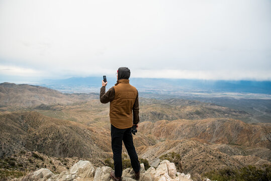 Man using phone on hill showing desert valleys below under gray sky