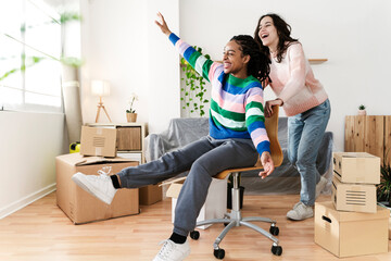 Carefree young woman pushing friend sitting in swivel chair at new home