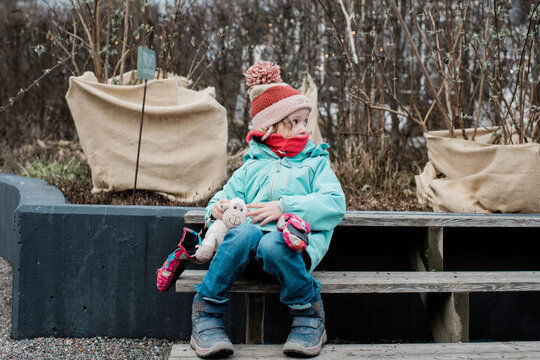 young girl wrapped up warm sitting with her toys in a garden in winter
