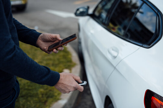 Man with mobile phone locking car with key
