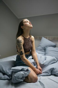 Woman with tattoo sitting on the bed.