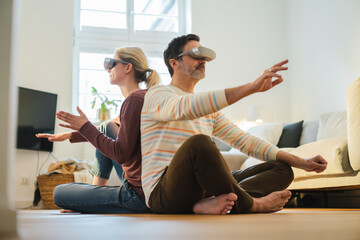Mature couple wearing wearing virtual reality headset and gesturing at home
