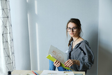 millennial girl draws fabulous images on paper while sitting at home